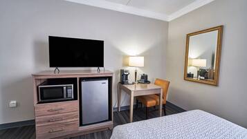 Ein Hotelzimmer mit einem Bett, einem Schreibtisch mit Stuhl, einem Fernseher, einer Mikrowelle, einem Kühlschrank, einer Lampe und einem Spiegel.