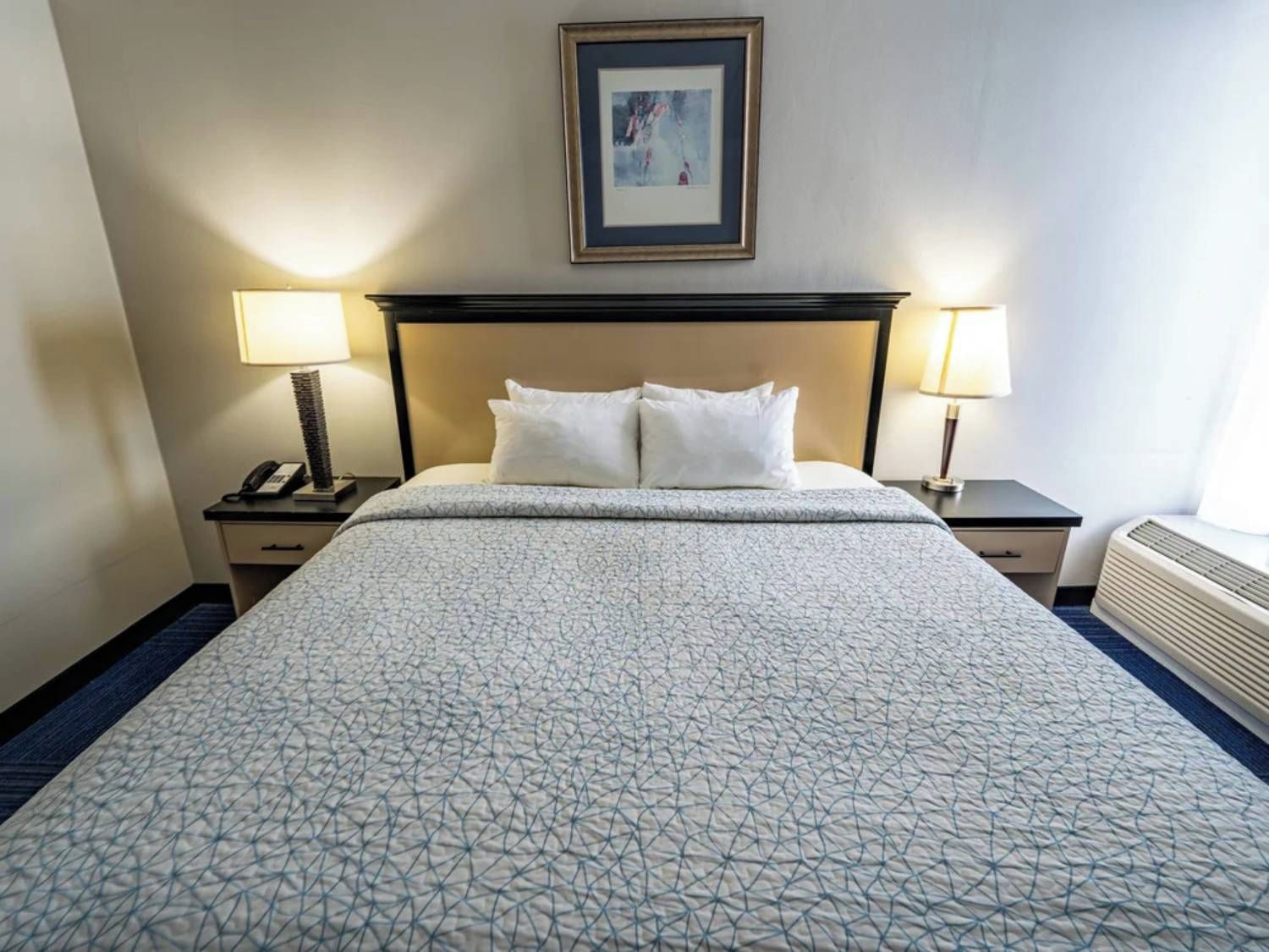 Quarto de hotel com cama, duas mesas de cabeceira, um quadro na parede e janela com vista.