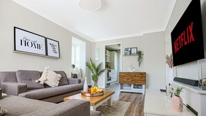 Uma sala de estar moderna com um sofá cinzento, uma mesa de centro de madeira com frutas, uma televisão na parede e uma estante de livros.