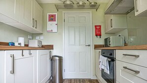 Uma cozinha compacta com armários brancos, uma lixeira de aço inoxidável, um micro-ondas e um forno.