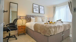 Quarto com cama, cadeira, mesa de cabeceira, espelho e duas fotos emolduradas na parede.