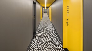 Un pasillo con piso de diseño geométrico, una puerta amarilla con el número 221 y una lámpara moderna.