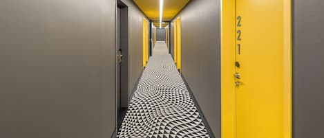 A hallway with a geometric patterned floor, a yellow door with the number 221, and a modern light fixture.