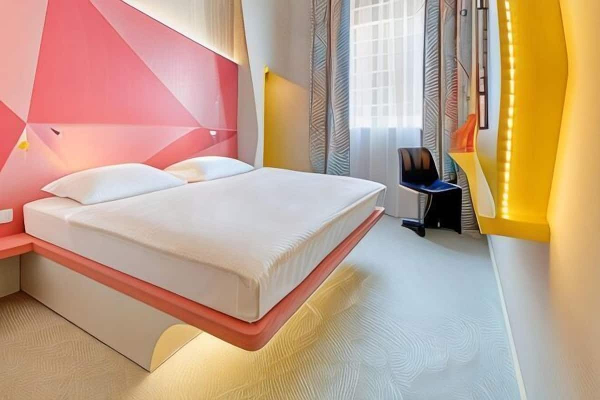 A modern hotel room with a bed, bedside table, and a window with curtains.