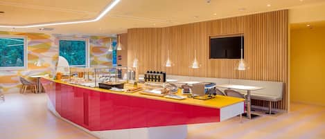 A modern hotel lobby with a central island counter, seating area, and a large TV screen.