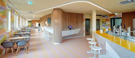 A modern hotel lobby with a long reception desk, bar area, and seating for guests.