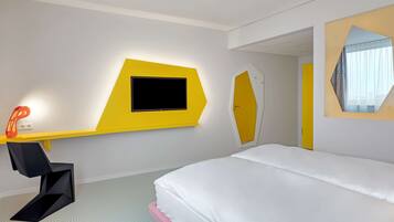 A modern hotel room with a bed, a desk with a flat-screen TV, and a mirror.