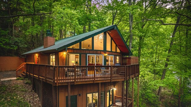 Een chalet met twee verdiepingen en een balkon, omgeven door dicht bos.