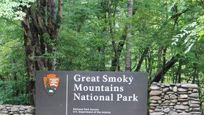 Een bord voor Great Smoky Mountains National Park, met een stenen muur en bomen op de achtergrond.
