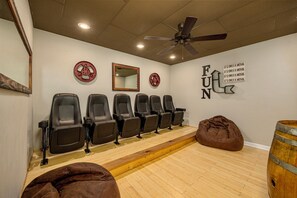A room with six black chairs aligned against a wall, a ceiling fan, a wooden barrel, and a brown bean bag.