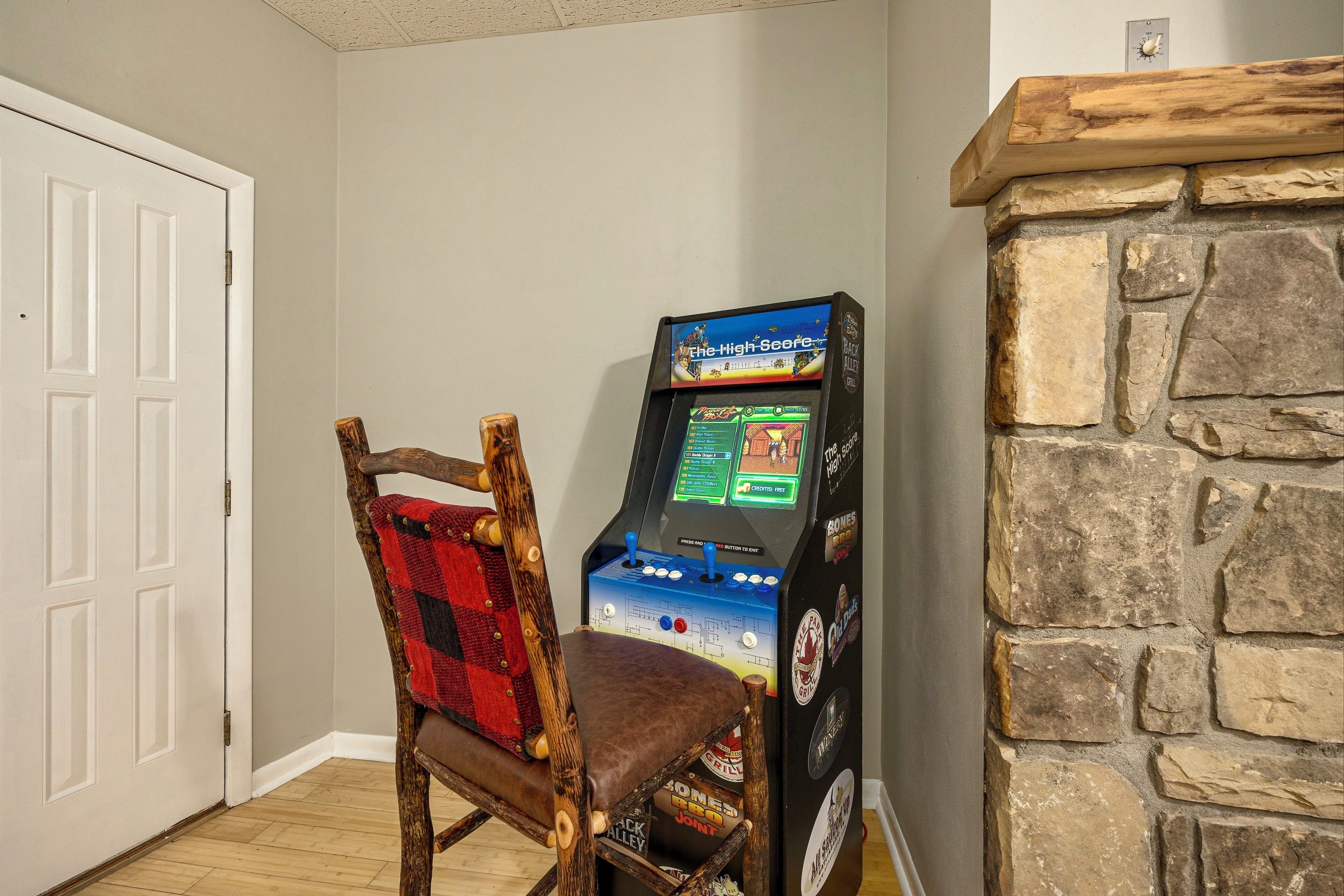 A wooden chair with a red and black checkered blanket, a video game console, and a stone fireplace.