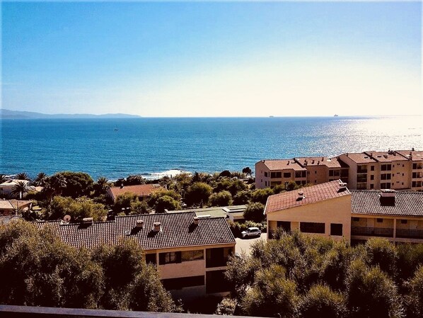 Un quartier résidentiel situé sur la côte, avec des bâtiments, une vue sur la mer et un navire visible au loin.