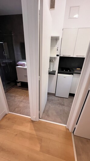 Une cuisine compacte avec des meubles blancs, un petit réfrigérateur et un four encastré.