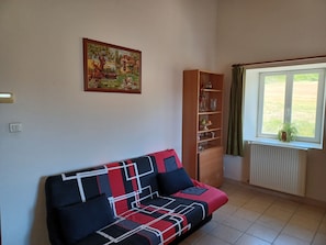 A living room with a sofa, a wooden cabinet, a radiator, and a window with a view of greenery.