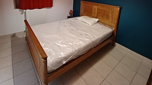 A bedroom with a wooden bed, a red curtain, a white mattress, and a hanging light fixture. - Type F2 apartment in a quiet country setting (Comps)