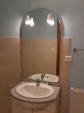 A bathroom with a sink, mirror, and two wall-mounted lights. - Type F2 Apartment in a Quiet Rural Setting   (Comps)