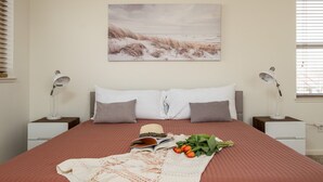Ein ordentlich bezogenes Bett mit einer braunen Tagesdecke, zwei Kissen, einem Hut, einem Buch und einem Blumenstrauß.
