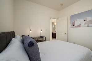 Restful retreat with a large bed, bedside table, and lamps, plus a door to a bathroom.