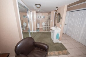 A bathroom with a toilet, sink, and mirror. There is a brown leather chair in the foreground.