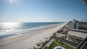 A beach view from a balcony with a clear sky, a sandy beach, and a building with a swimming pool. - Spacious 9th floor Horizons Oceanfront 2/2 (Daytona Beach)