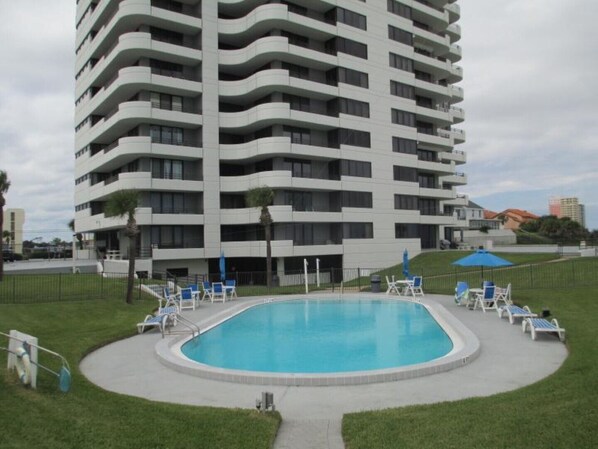 A modern multi-story building with a swimming pool and lounge chairs.