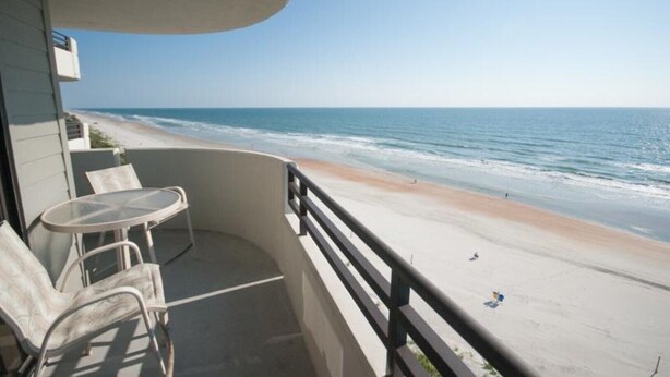 A balcony with a table and chairs overlooking a beach. - Spacious 9th floor Horizons Oceanfront 2/2 (Daytona Beach)