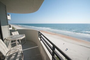 Ein Balkon mit Tisch und Stühlen mit Blick auf einen Strand.