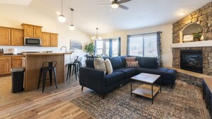A spacious living area with a dark-colored sectional sofa, a small coffee table, and a fireplace. There is a kitchen area with wooden cabinets and a microwave. - Heber House, 20 min to Park City! Close to downtown Heber. (Heber City)