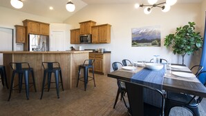 A modern kitchen with wooden cabinets, a central island with bar stools, a dining area with a table set for four, and a large window with a mountain view. - Heber House, 20 min to Park City! Close to downtown Heber. (Heber City)