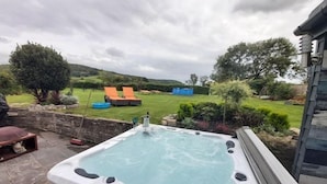 A hot tub in a backyard with a stone wall, a lawn, and a view of the countryside. - Bluebell House 5 Star Luxury 4 Bdrms and hot tub (Somerton)