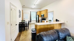 A modern kitchen with wooden cabinets, a central island, and a dining area with a table and chairs. - Chateau 8, spacious townhouse in Tickfaw, LA (Tickfaw)