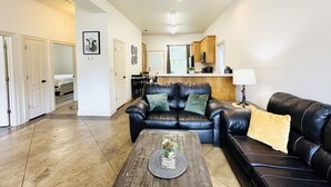 A spacious living room with a black leather sofa, a coffee table with a decorative item, and a kitchen area in the background. - Chateau 8, spacious townhouse in Tickfaw, LA (Tickfaw)