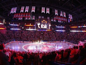 A large indoor arena with a hockey rink, surrounded by a packed audience.
