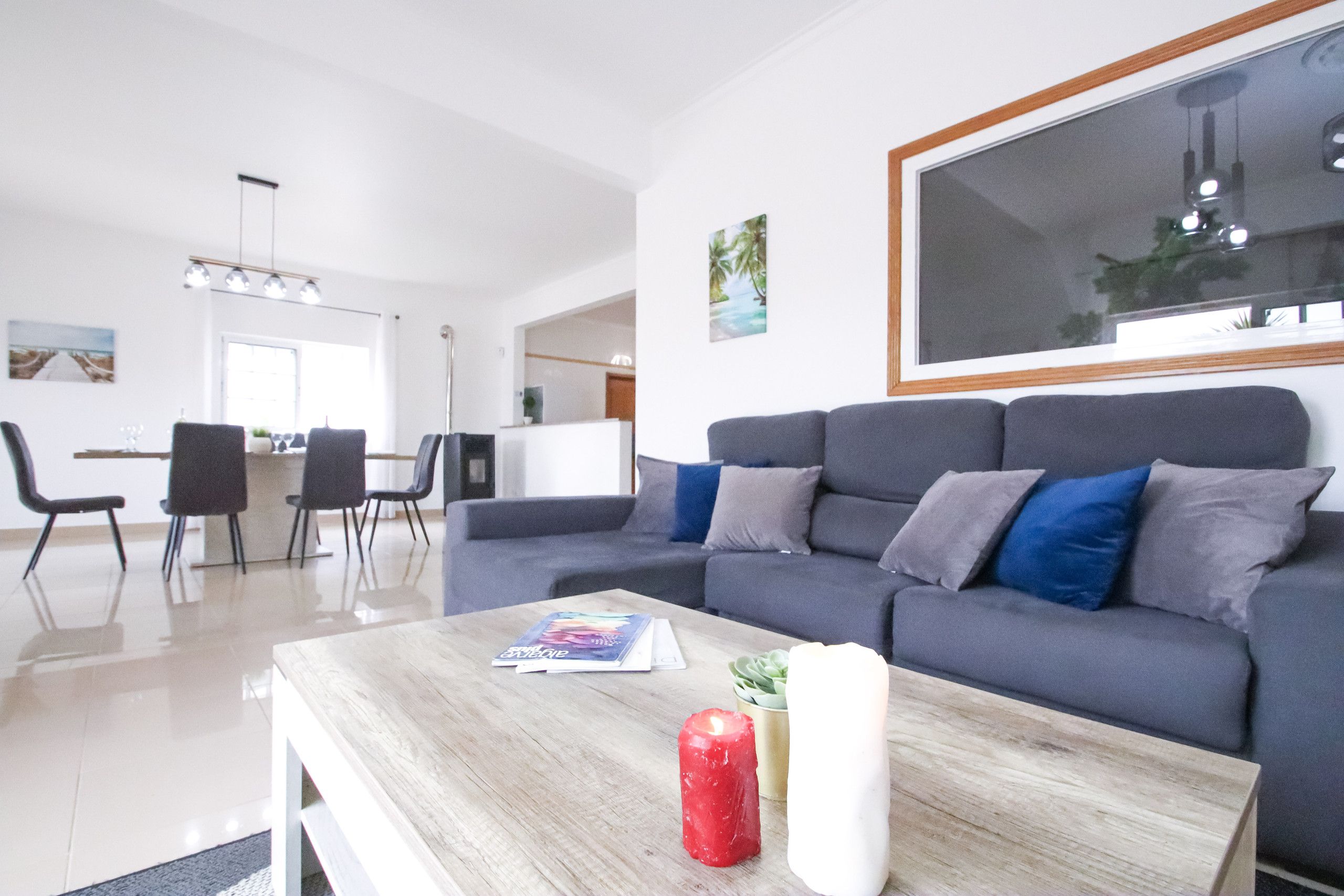 Una sala de estar moderna con un sofá gris, una mesa de centro de madera y un comedor al fondo.