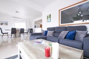A modern living room with a grey sofa, a wooden coffee table, and a dining area in the background.