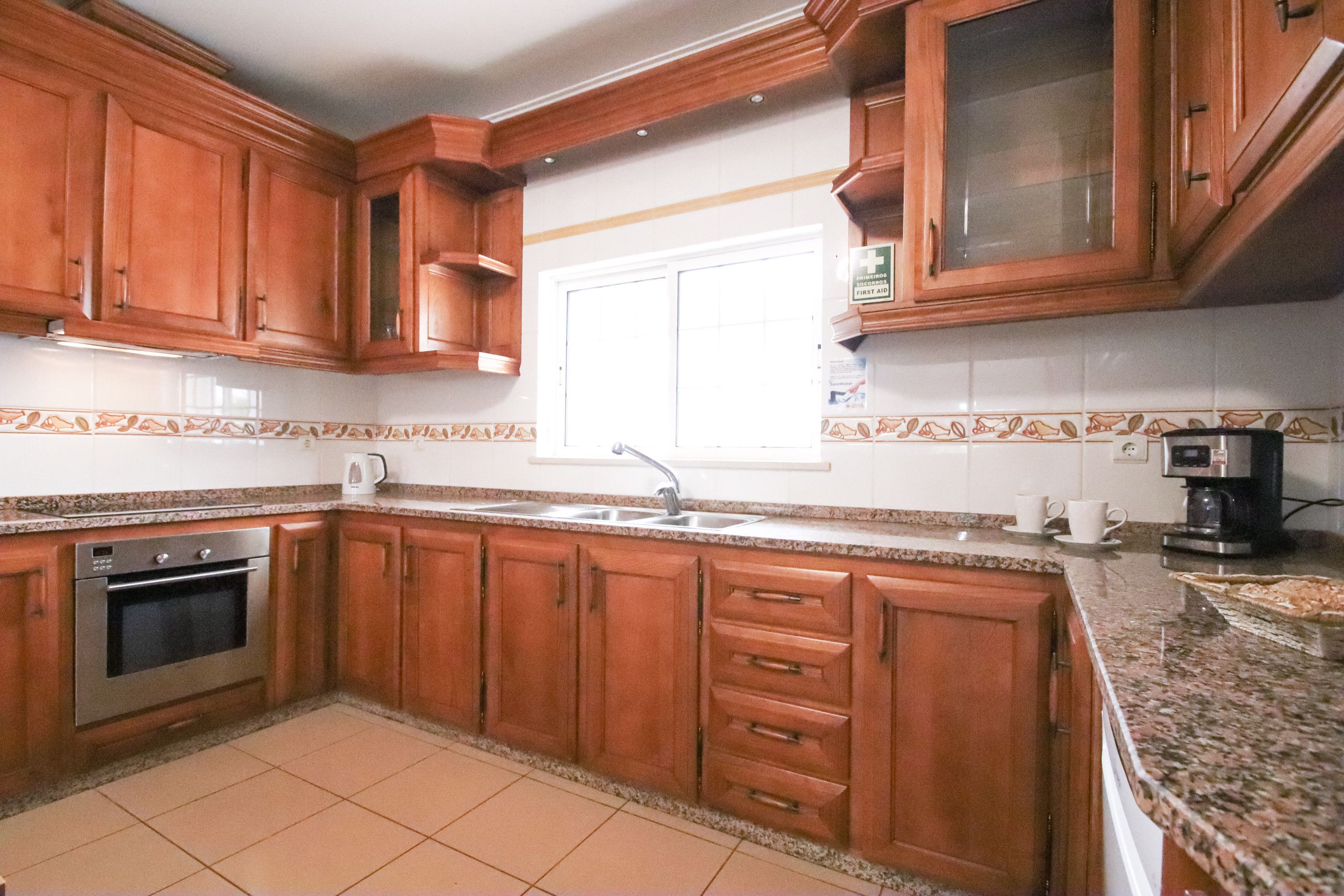 Una cocina con armarios de madera, un horno de acero inoxidable, un fregadero y una cafetera.