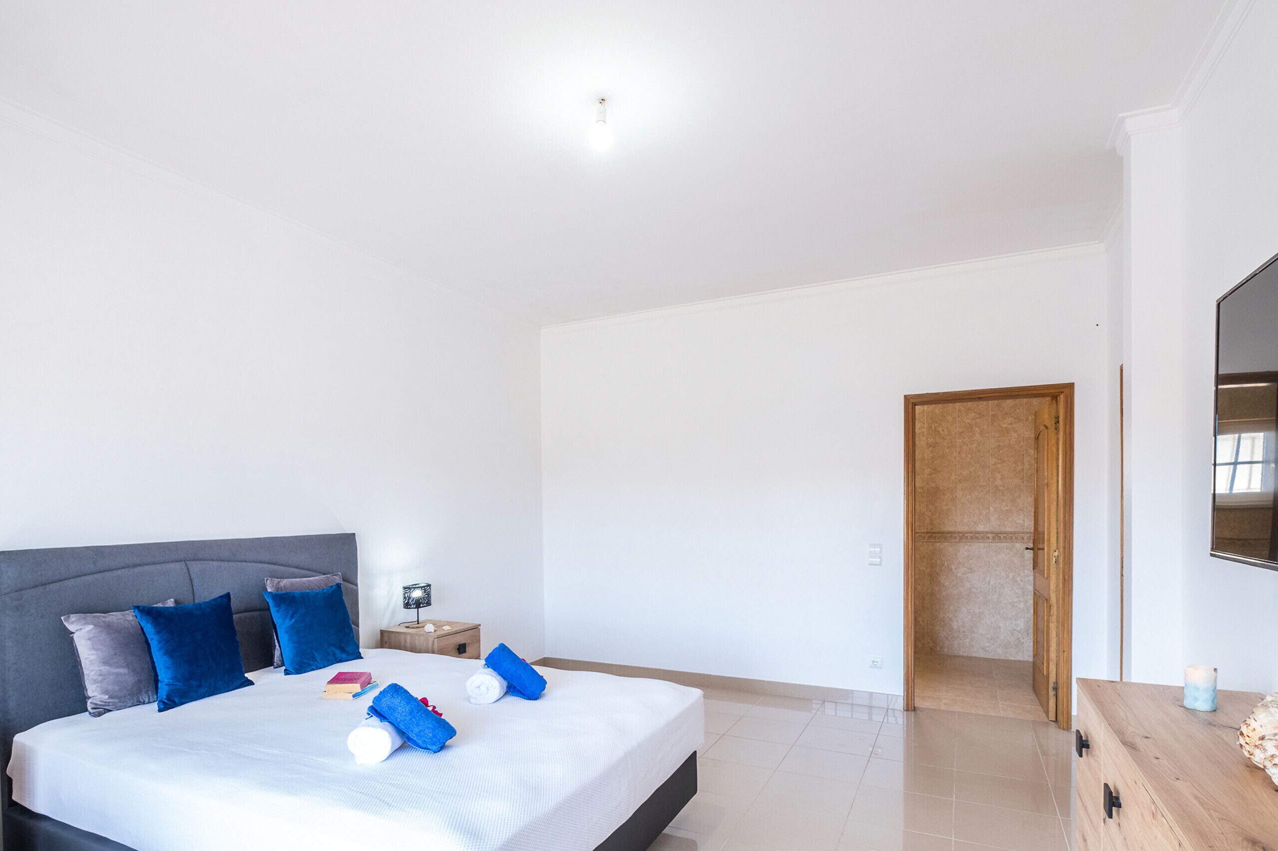 Una habitación de hotel moderna con una cama grande, una mesita de noche, un televisor y una puerta de madera que da a un baño.