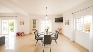A spacious dining area with a long table, chairs, and a television on the wall. - Villa with Saltwater Swimming Pool (Albufeira)