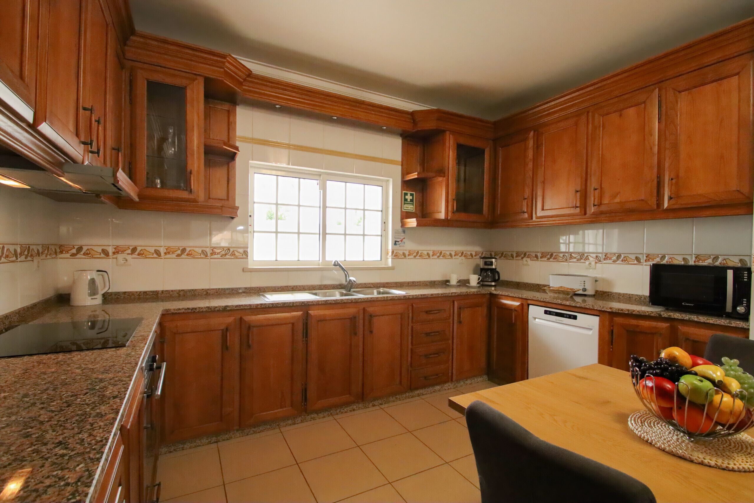 Una cocina con armarios de madera, una ventana, un lavamanos, una cafetera, un microondas y un frutero sobre la encimera.
