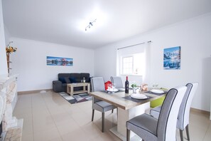 A modern living room with a dining area, featuring a sofa, a coffee table, and a dining table set for two.