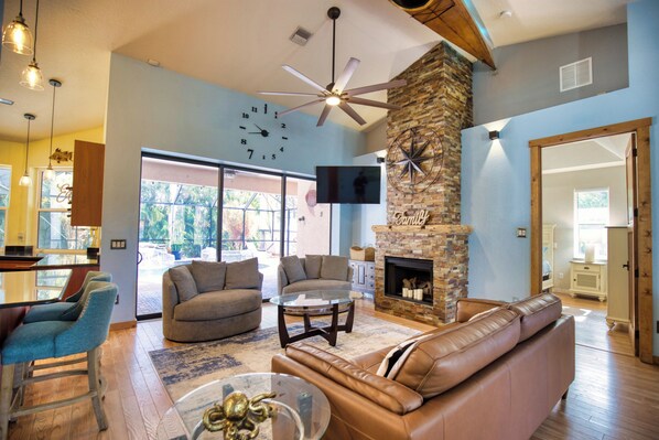 A spacious living room with a stone fireplace, leather sofa, and a ceiling fan. - Spacious 3 Br Home w/ Pool- 1 mile walk to beach (Nokomis)