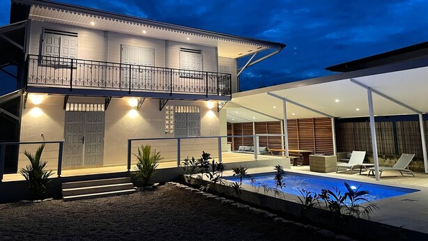 Una casa a due piani con un balcone, una piscina e un'area salotto esterna.