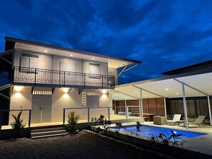 Une maison à deux étages dotée d’un balcon, d’une piscine et d’un espace salon extérieur.