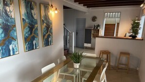 Un'area pranzo moderna con tavolo in vetro e sedie bianche, una cucina sullo sfondo e dipinti astratti alle pareti.