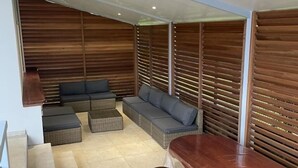 Un interno moderno con una parete a listelli di legno, un divano modulare grigio, una panca di legno e un pavimento piastrellato.