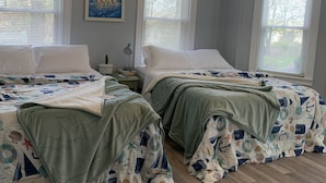A bedroom with two beds, a nautical-themed bedspread, a chandelier, and a painting of sailboats.