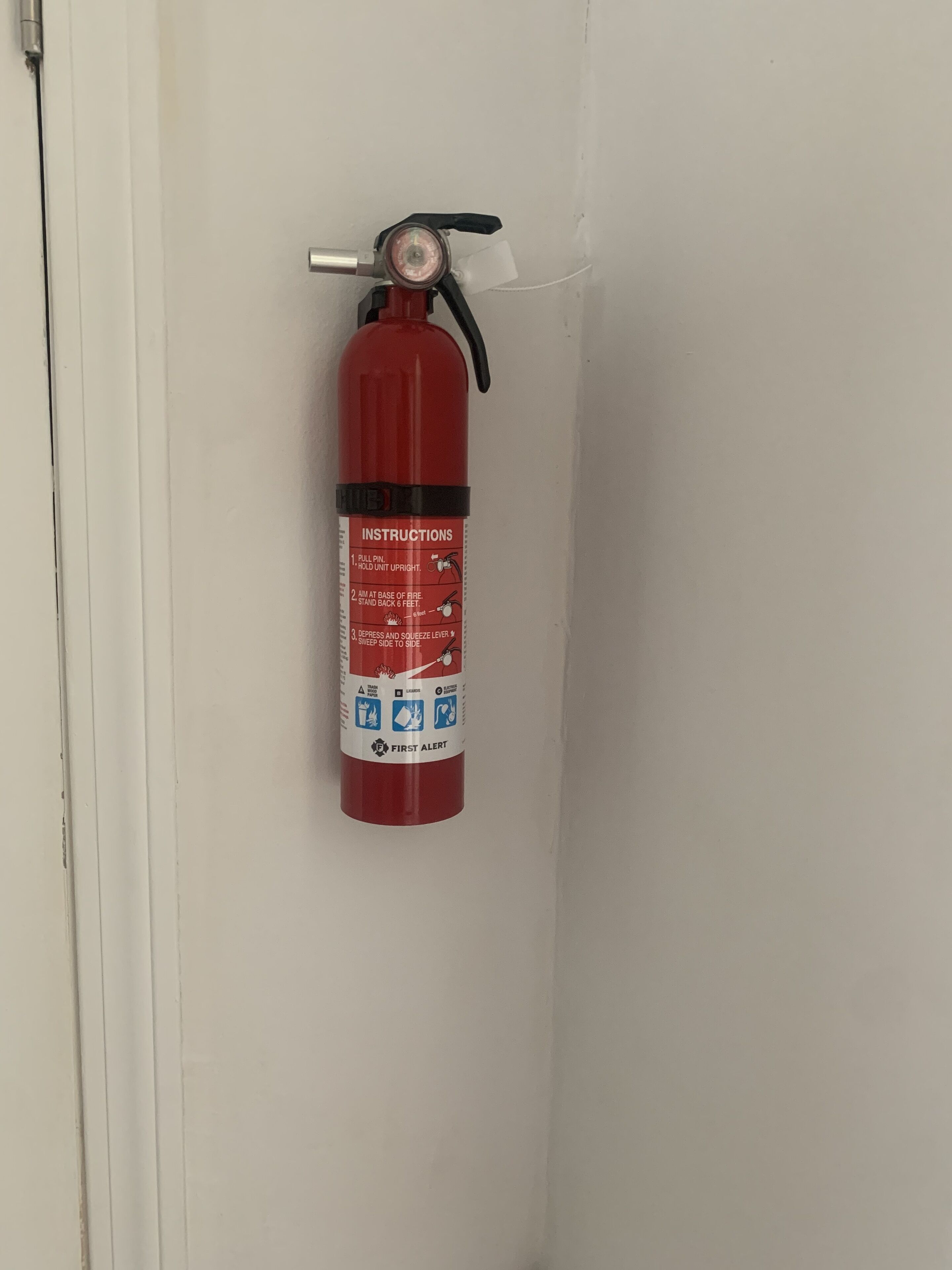 Extintor rojo sujeto a una pared blanca cerca de una puerta.