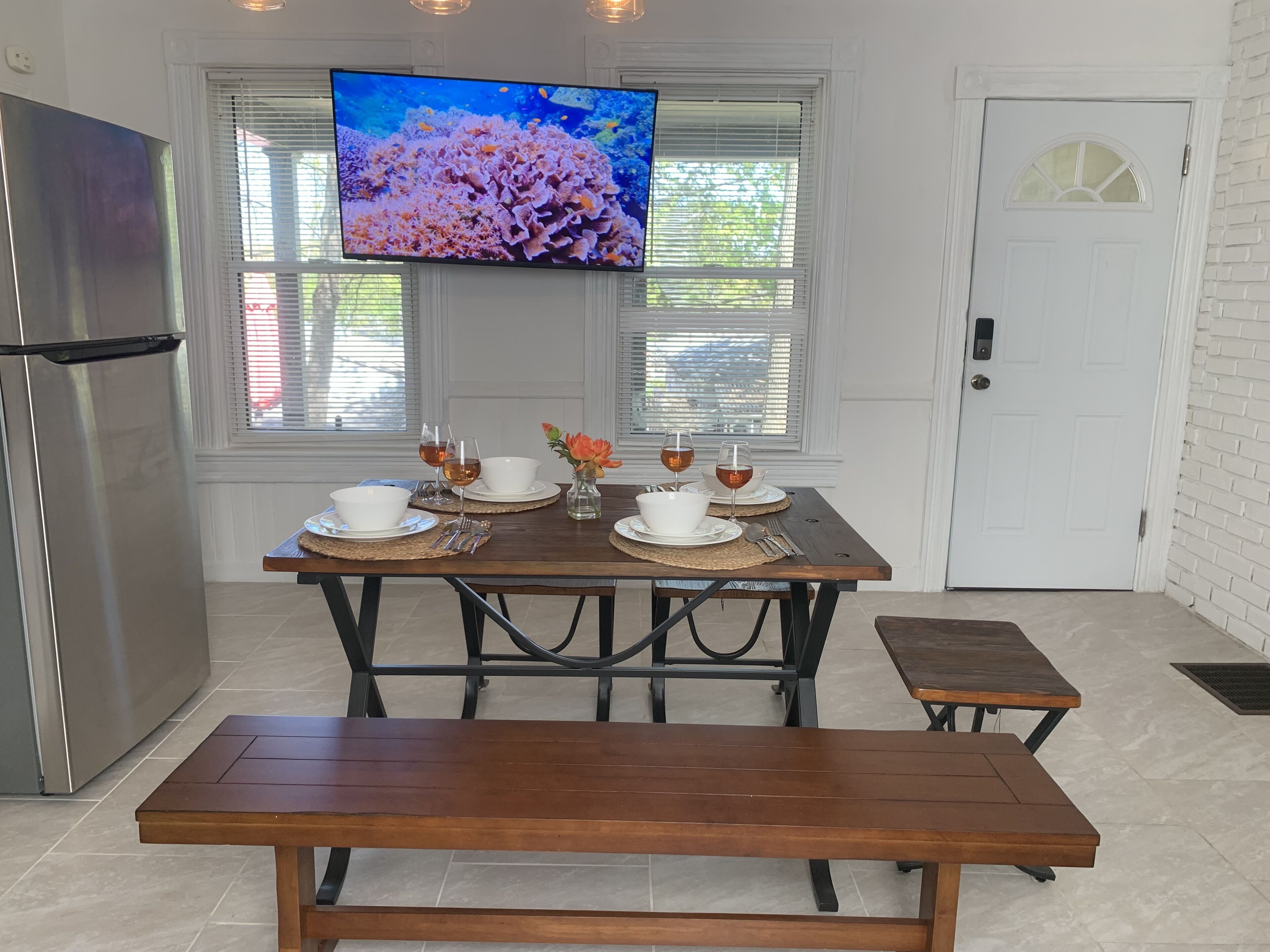 A dining area with a wooden table set for two, a bench, and a TV mounted above the table displaying an underwater scene.