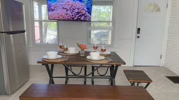 A dining area with a wooden table set for two, a bench, and a TV mounted above the table displaying an underwater scene.