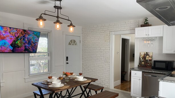 A modern kitchen with white brick walls, a dining area with a wooden table and benches, and a TV mounted on the wall.